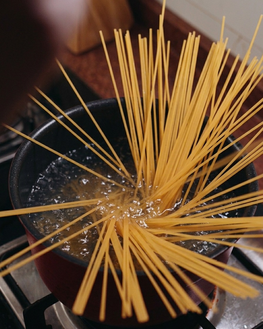 Spaghetti secchi inseriti verticalmente in una pentola di acqua bollente che si aprono a ventaglio.