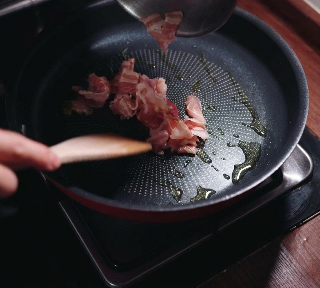 Pezzi di guanciale versati da una ciotola in una padella nera con un po dolio.