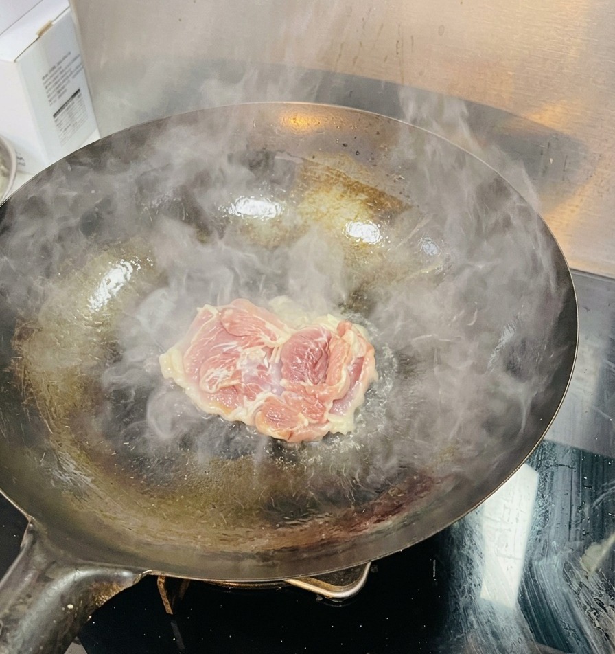 Una coscia di pollo cruda inserita in un wok ben caldo con vapore visibile e olio sfrigolante.