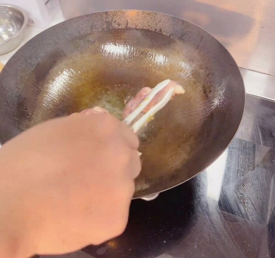 Un paio di pinze che gira una coscia di pollo in un wok scuro, mostrando la pelle croccante e dorata.