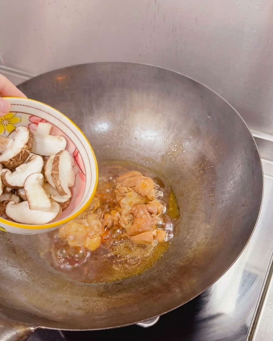 Funghi shiitake freschi a fette aggiunti da una ciotola in un wok contenente pollo rosolato e salsa in ebollizione.