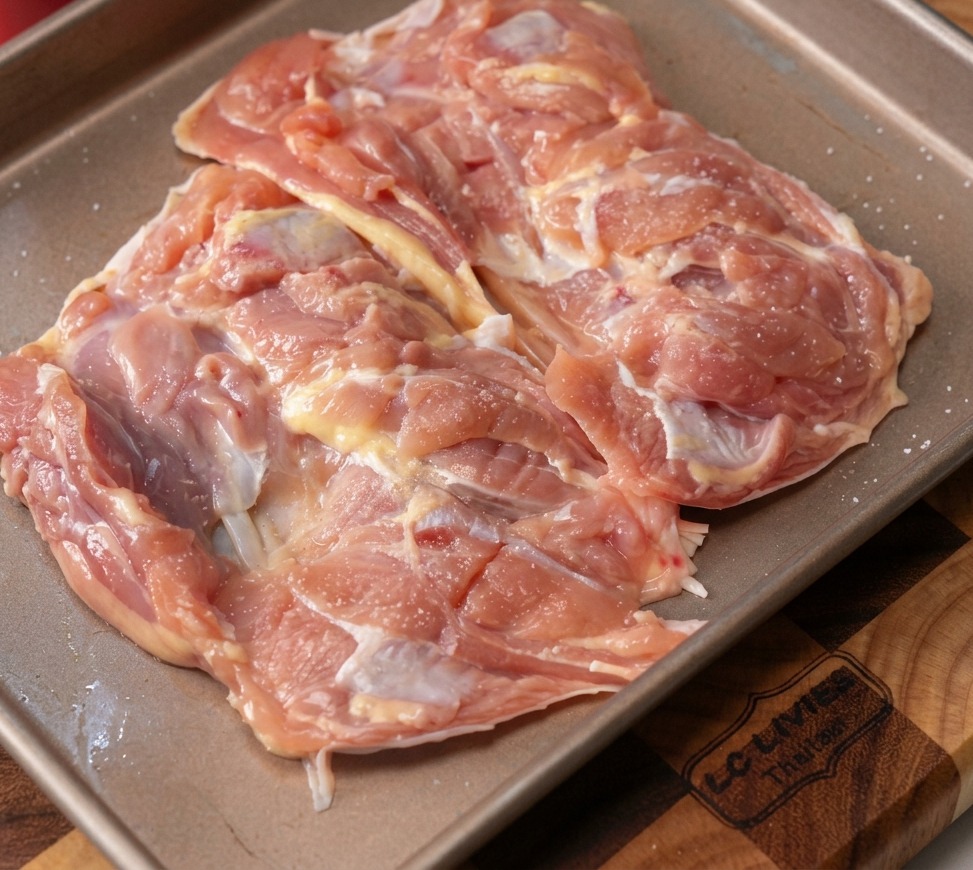 Sovracosce di pollo crude e disossate su una teglia di metallo, cosparse di aglio tritato e pepe nero.