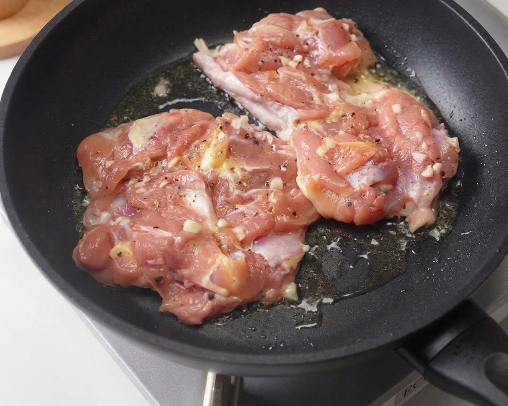 Due sovracosce di pollo marinate che rosolano con il lato della pelle rivolto verso il basso in una padella antiaderente scura.