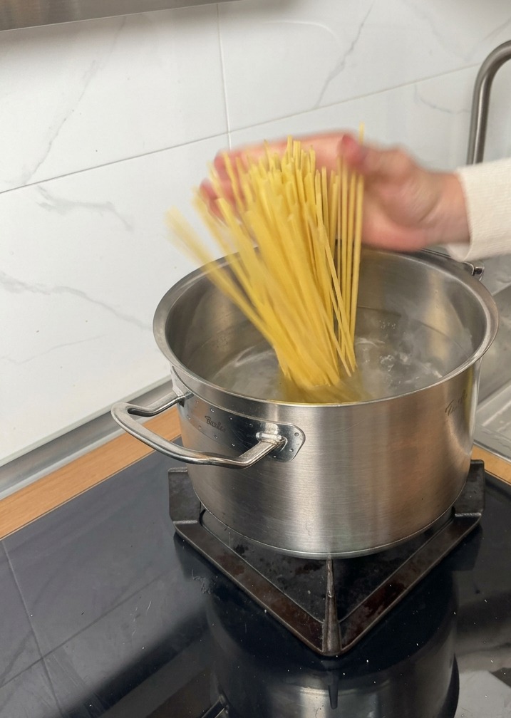 Pasta lunga secca aggiunta a una pentola di acqua bollente su un piano a induzione.