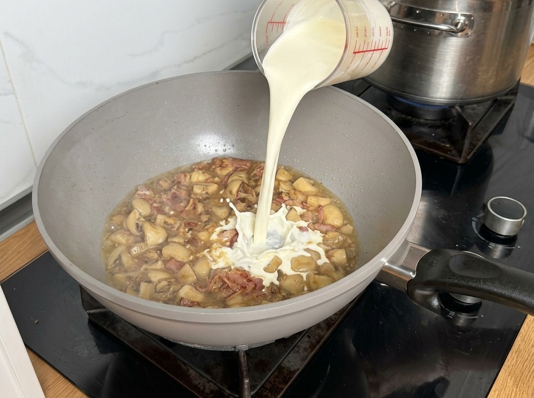 Panna fresca versata nella padella che crea un leggero schizzo colpendo la base di funghi.