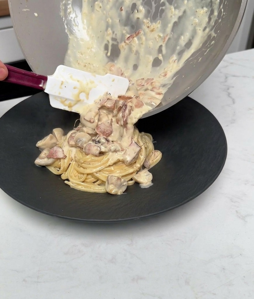 Versare la salsa rimasta, i funghi e la pancetta dalla padella sopra la pasta impiattata.