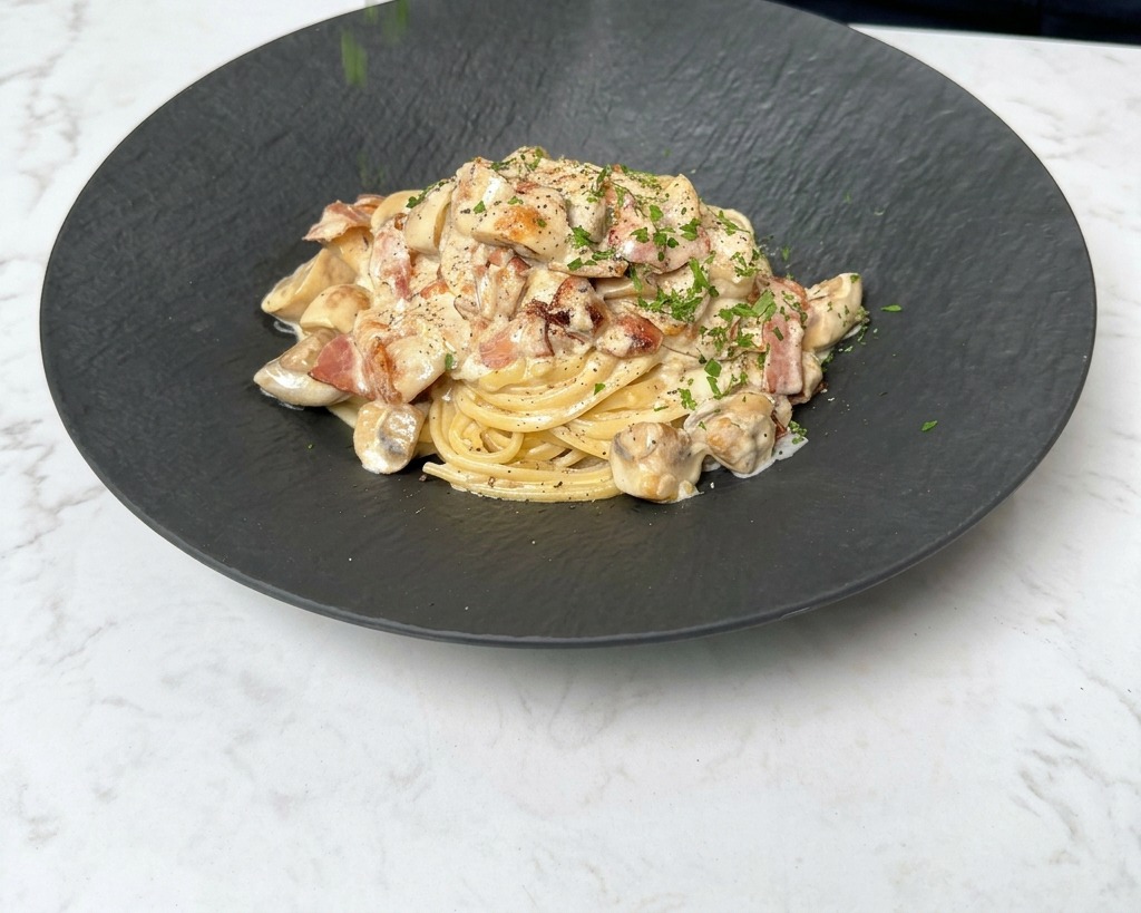 Prezzemolo fresco tritato spolverato sopra un piatto fumante di pasta cremosa con pancetta e funghi.