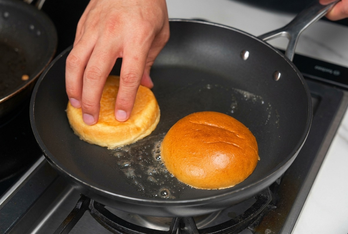 Metà di panini per hamburger tostati a faccia in giù in una padella con burro fuso sfrigolante.