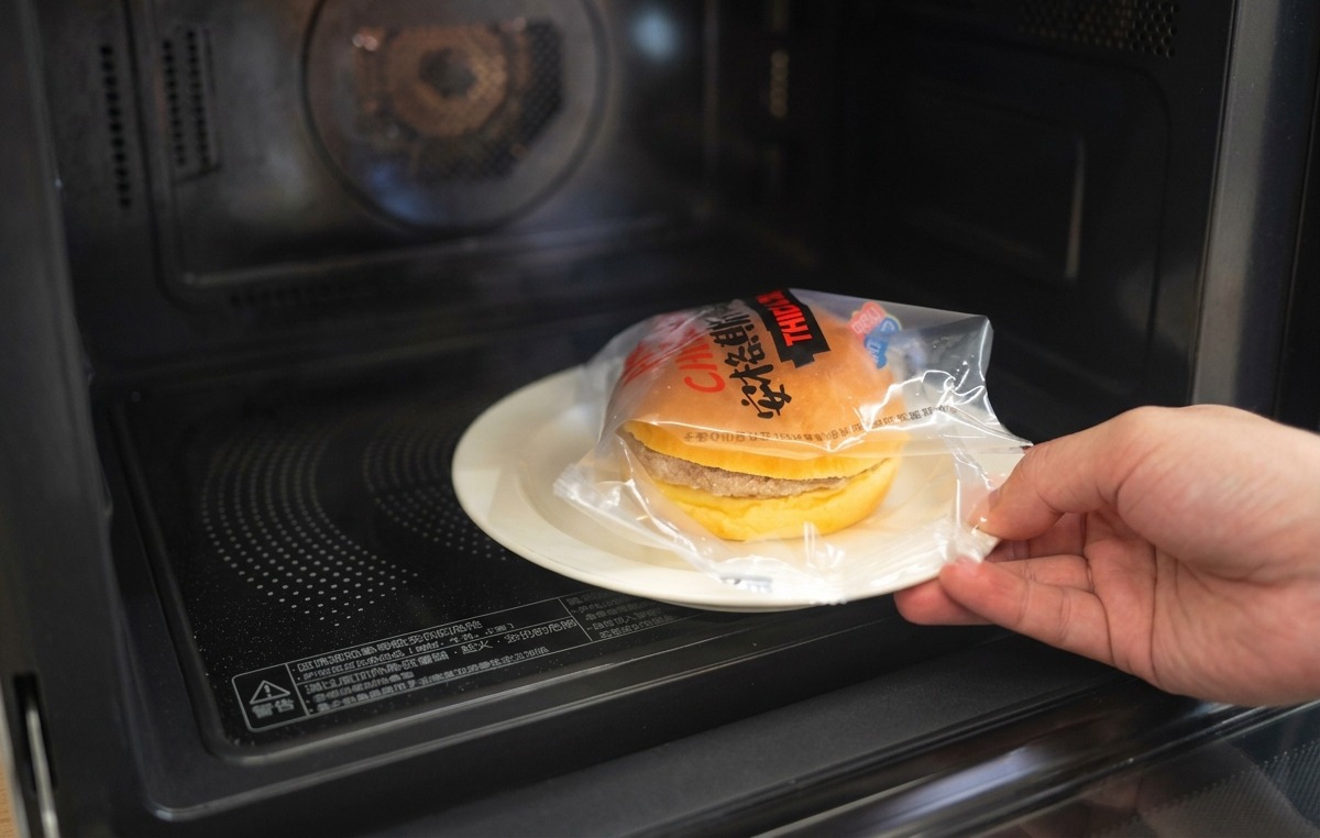 Una mano che posiziona la metà superiore di un panino brioche tostato su un hamburger ricoperto di cipolle e formaggio fuso.