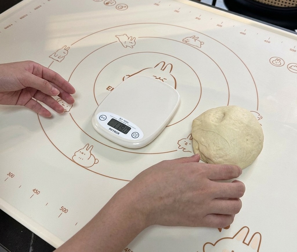 Una piccola porzione di impasto che riposa su un tappetino da forno accanto a una bilancia digitale che ne indica il peso.
