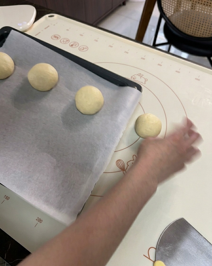 Una mano che posiziona le palline di impasto tonde su una teglia nera rivestita di carta da forno bianca.