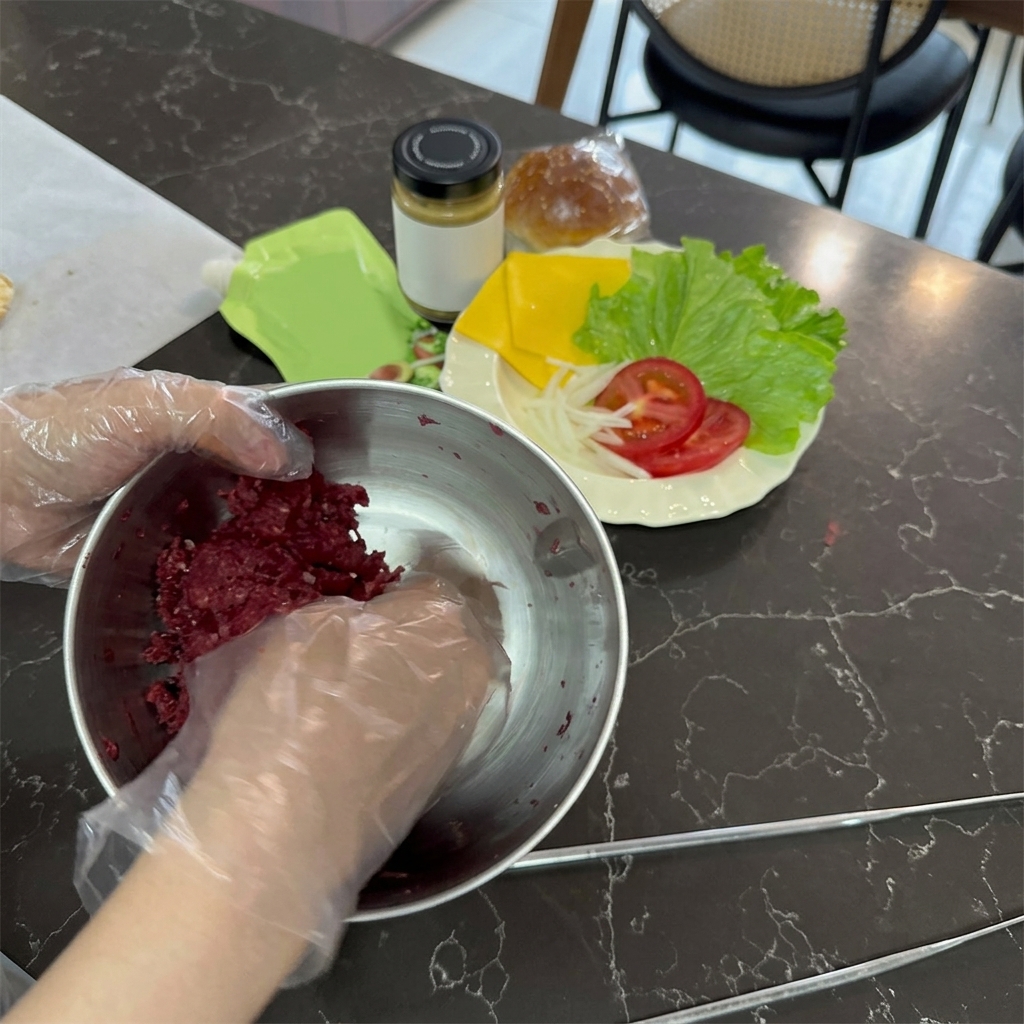 Mani che indossano guanti di plastica trasparenti mentre mescolano carne di manzo macinata cruda e rossa in una ciotola di acciaio inossidabile.