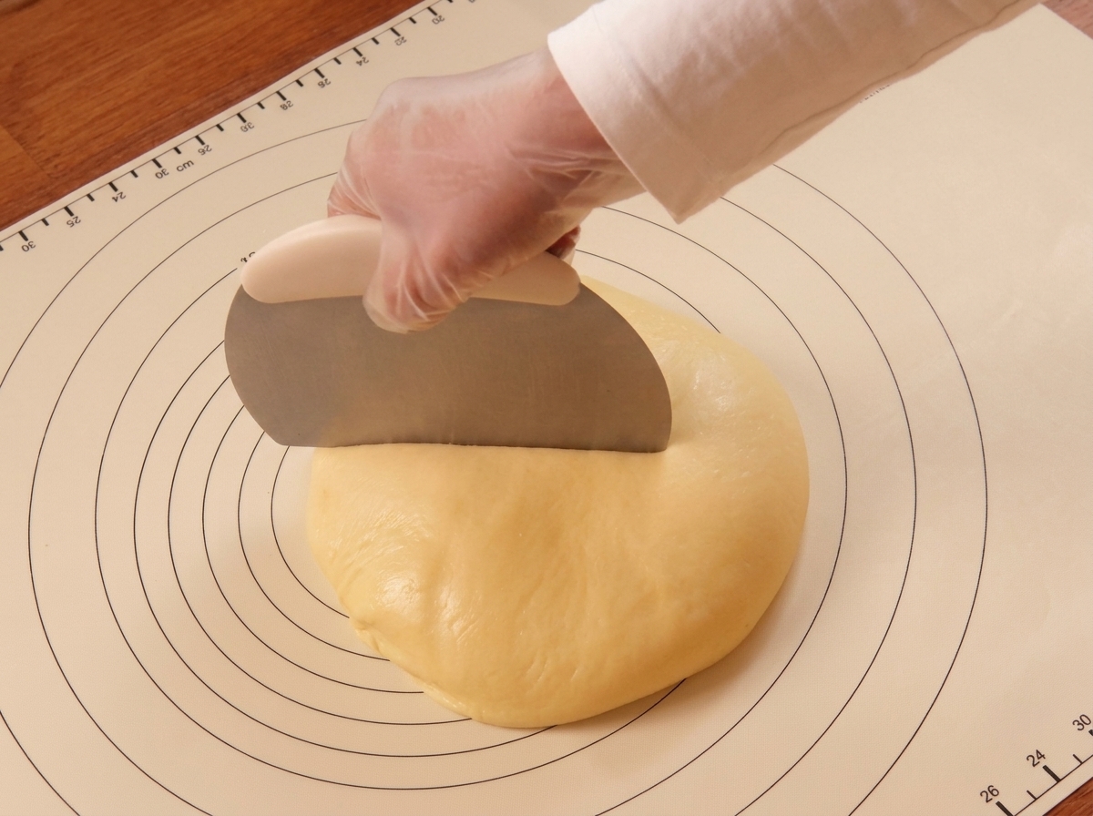 Una mano usa un tarocco di metallo per dividere limpasto su un tappetino in silicone.