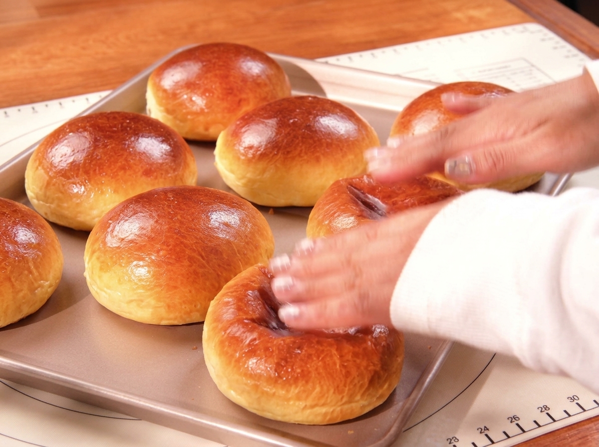 Panini brioche appena sfornati, lucidi e dorati, su una teglia da forno.