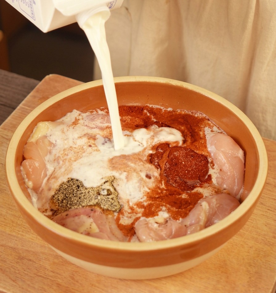 Latte fresco versato da un cartone in una ciotola con sovracosce di pollo condite.