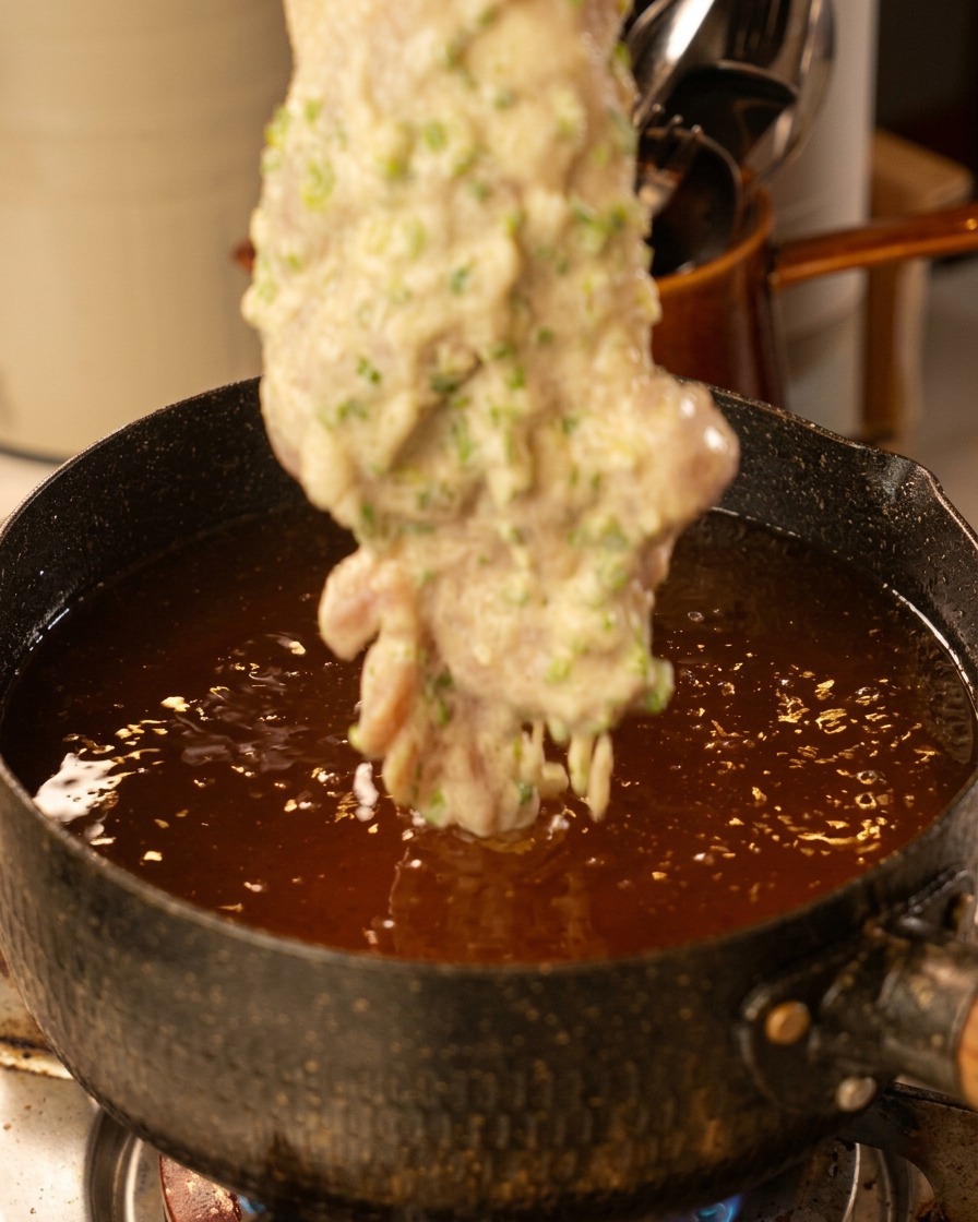Una sovracoscia di pollo impastellata immersa in una pentola di olio bollente.