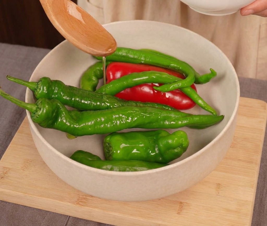 Olio di semi versato da un cucchiaio di legno su un mix di peperoncini freschi rossi e verdi in una ciotola chiara.
