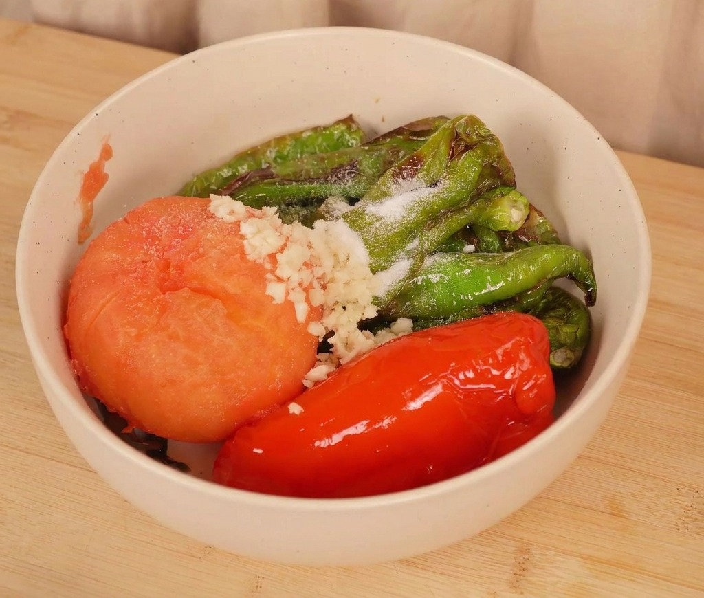 Una ciotola di peperoncini e pomodoro arrostiti con sopra aglio tritato fresco e un pizzico di sale.