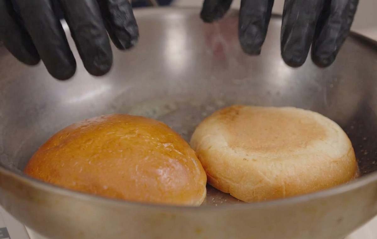 Mani con guanti neri che premono le metà del panino su una padella calda con burro fuso.