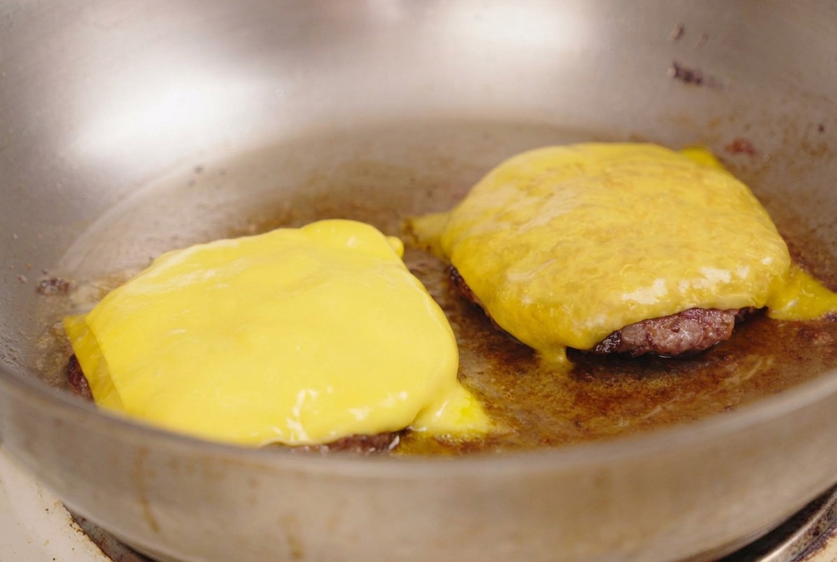 Fette di formaggio giallo che si fondono sopra le polpette di carne in padella.
