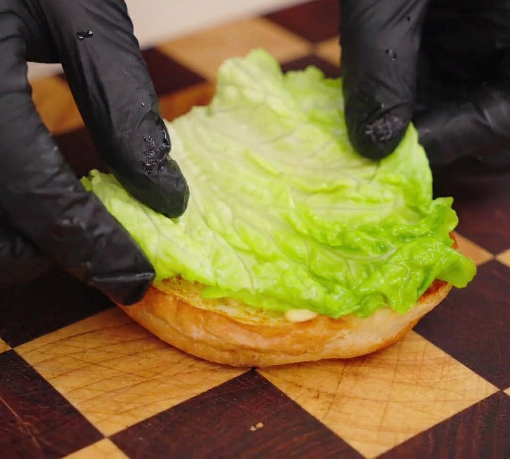 Persona che posiziona una foglia di lattuga fresca sulla base di un panino tostato.