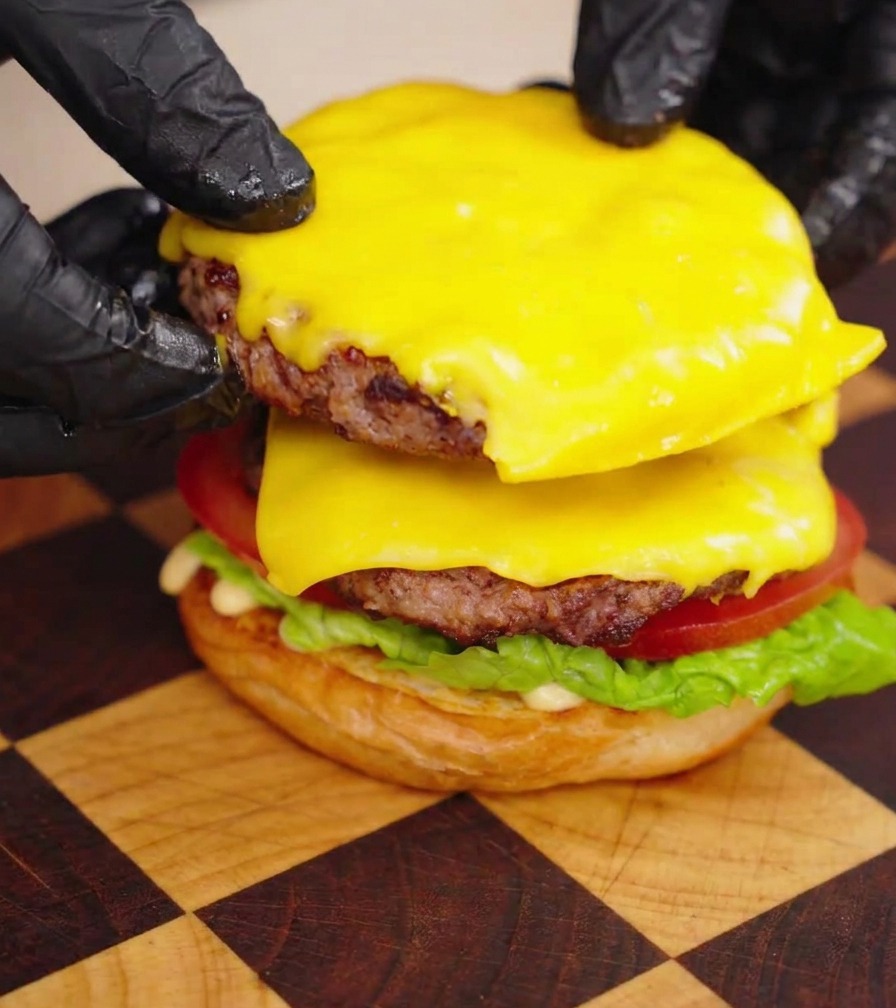 Mani che impilano due polpette di Wagyu con formaggio fuso sulla base del burger.