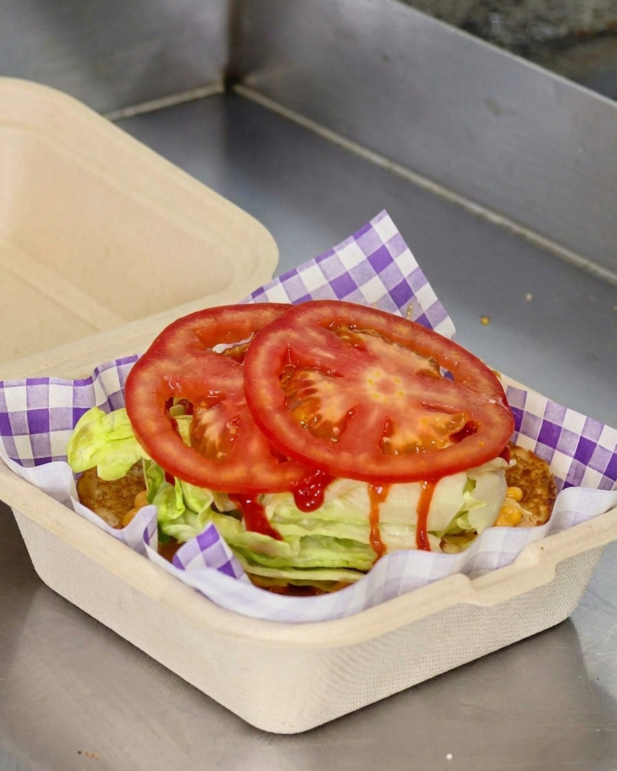 Due fette tonde di pomodoro rosso fresco posizionate sopra la lattuga in un contenitore da asporto.