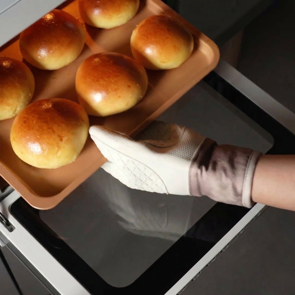 Una mano con un guanto bianco che estrae una teglia di panini brioche dorati dal forno caldo.