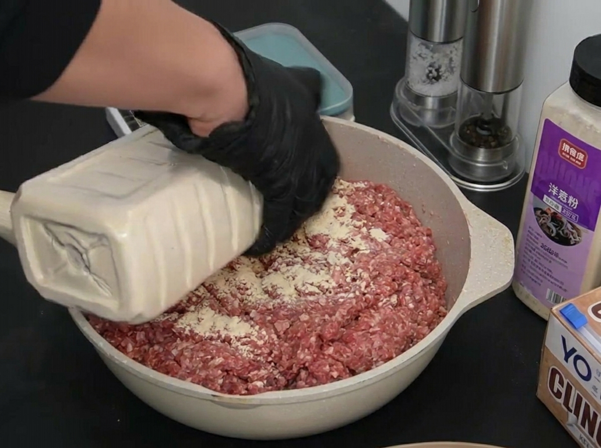 Una persona con guanti neri versa aglio in polvere sopra la carne di manzo cruda.