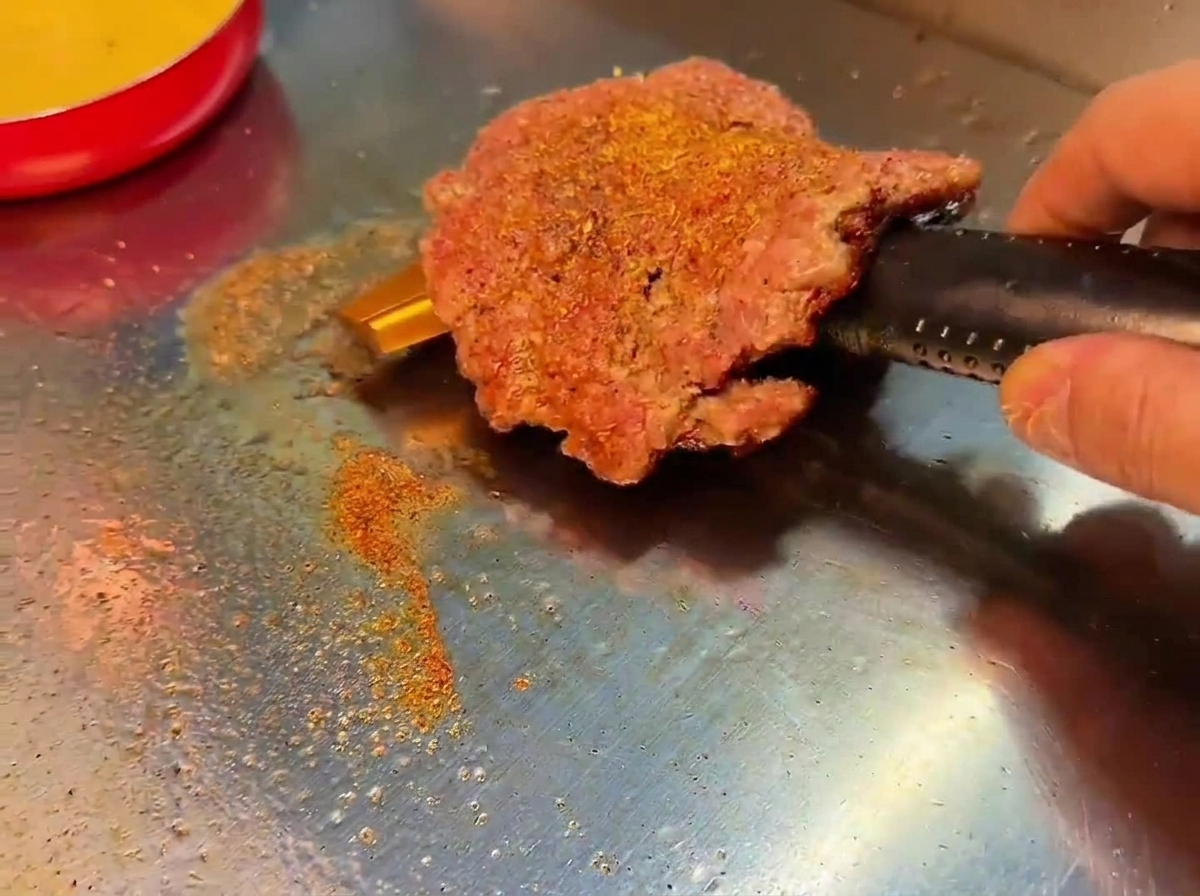 Un patty di manzo girato sulla piastra che rivela una crosticina scura e saporita.