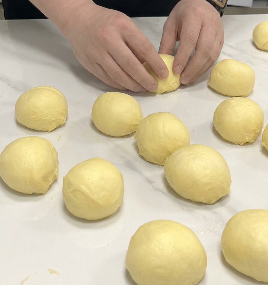 Mani che formano palline di impasto brioche su un piano di marmo bianco.