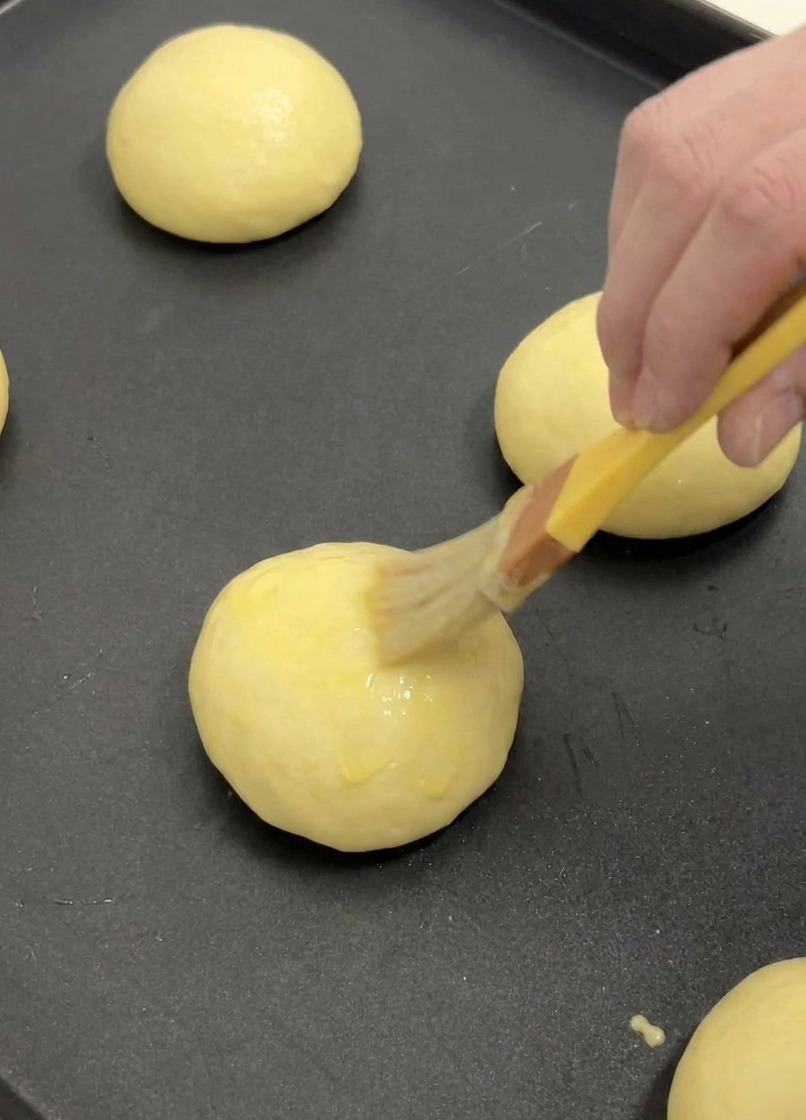 Pennello da cucina che applica uno strato sottile di uovo sbattuto sulla cima di un panino brioche lievitato.