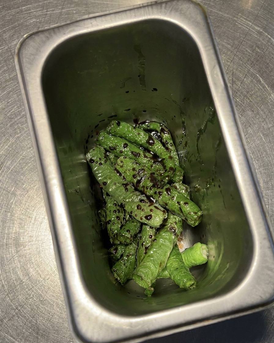 Peperoncini verdi fritti in un contenitore, ricoperti da una miscela scura di aceto e soia.