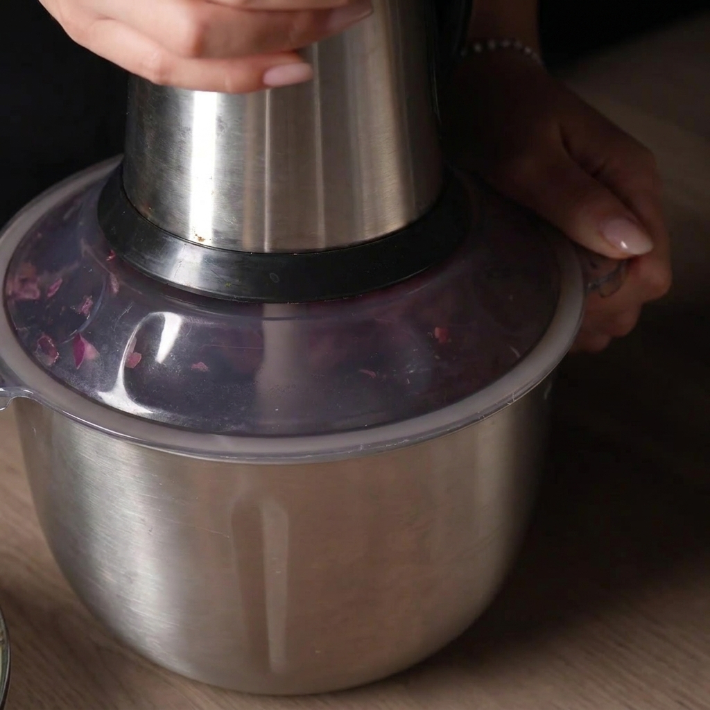 Mano che preme il coperchio di un robot da cucina per frullare a impulsi la carne cruda allinterno.