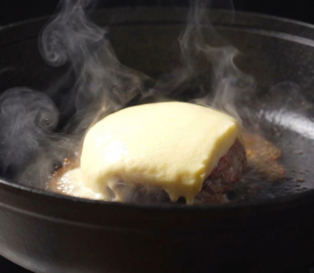 Fetta di formaggio che si scioglie sopra un burger in una padella di ghisa fumante.