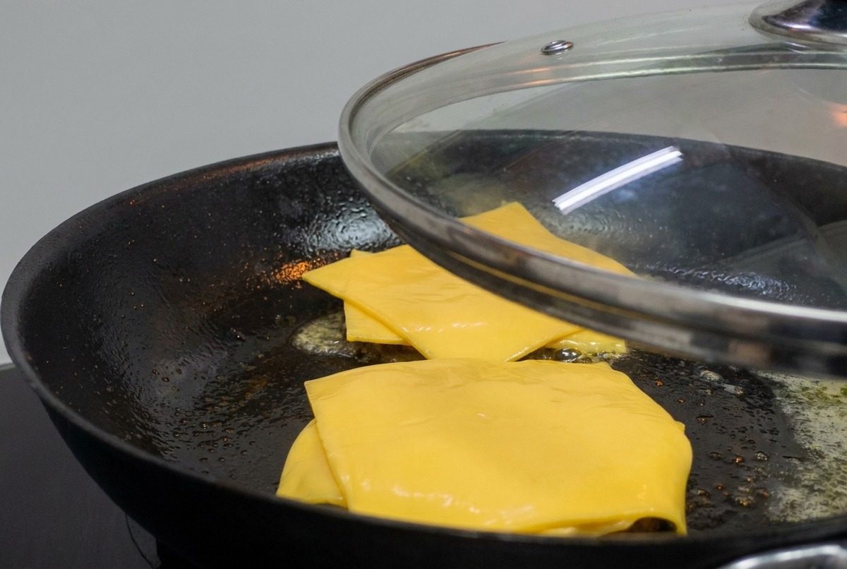 Un coperchio di vetro posizionato sopra una padella con burger e formaggio fuso.