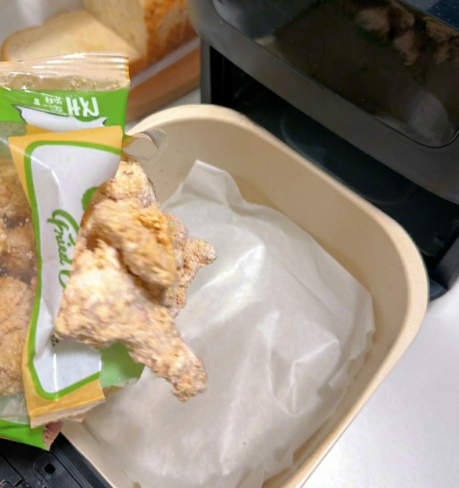 Pezzi di pollo impanato surgelati versati in un cestello della friggitrice ad aria foderato con carta forno bianca.
