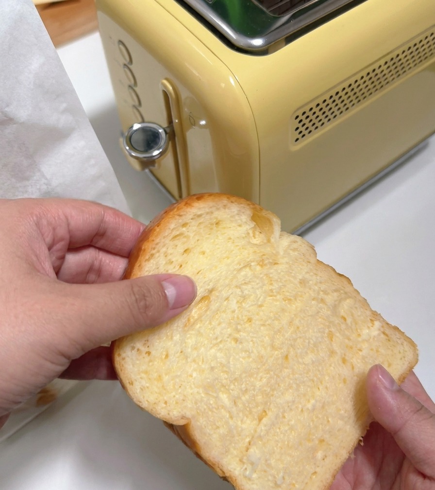 Una persona che inserisce una fetta spessa di pane bianco in un tostapane giallo in stile retrò.