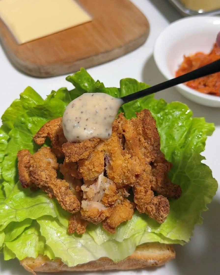 Un cucchiaio di maionese cremosa allo yuzu e pepe versato sopra il pollo fritto tagliato a pezzi su un letto di lattuga.