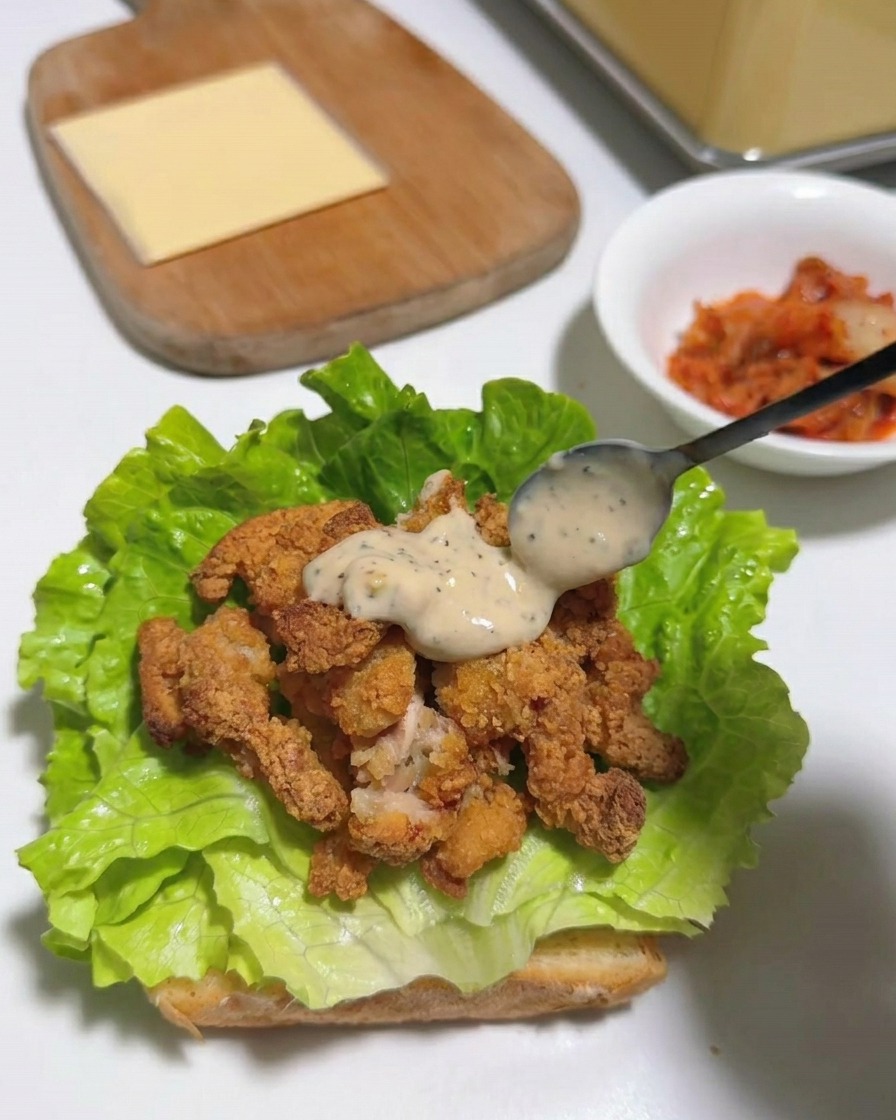 Una fetta quadrata di formaggio giallo adagiata sopra le strisce di pollo condite e la lattuga.