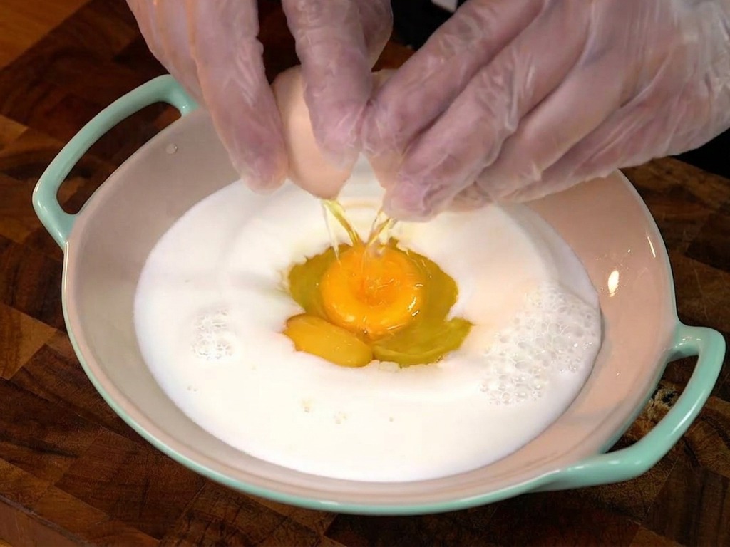Qualcuno rompe un uovo in una ciotola di latte.