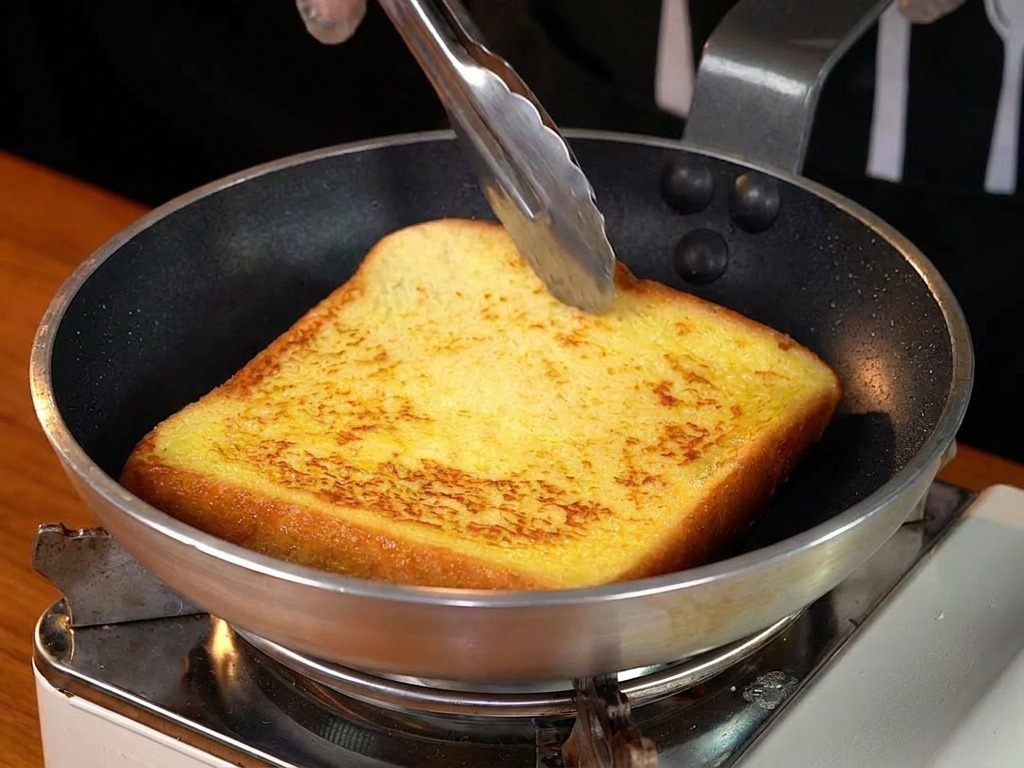 Una fetta dorata di French toast viene girata in padella con delle pinze.