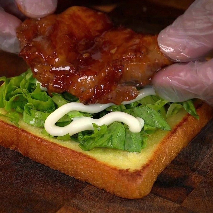 Mani posizionano il pollo caramellato sulla base del sandwich con lattuga e maionese.