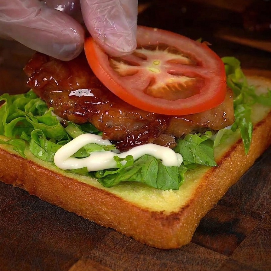 Una mano mette una fetta di pomodoro fresco sopra il pollo laccato.