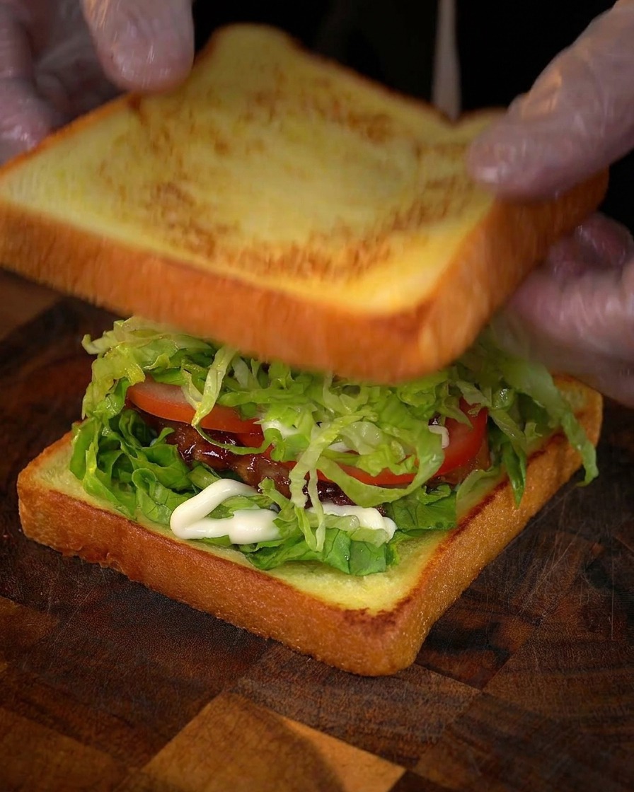 Mani che posizionano la fetta finale di pane tostato sopra il sandwich farcito.