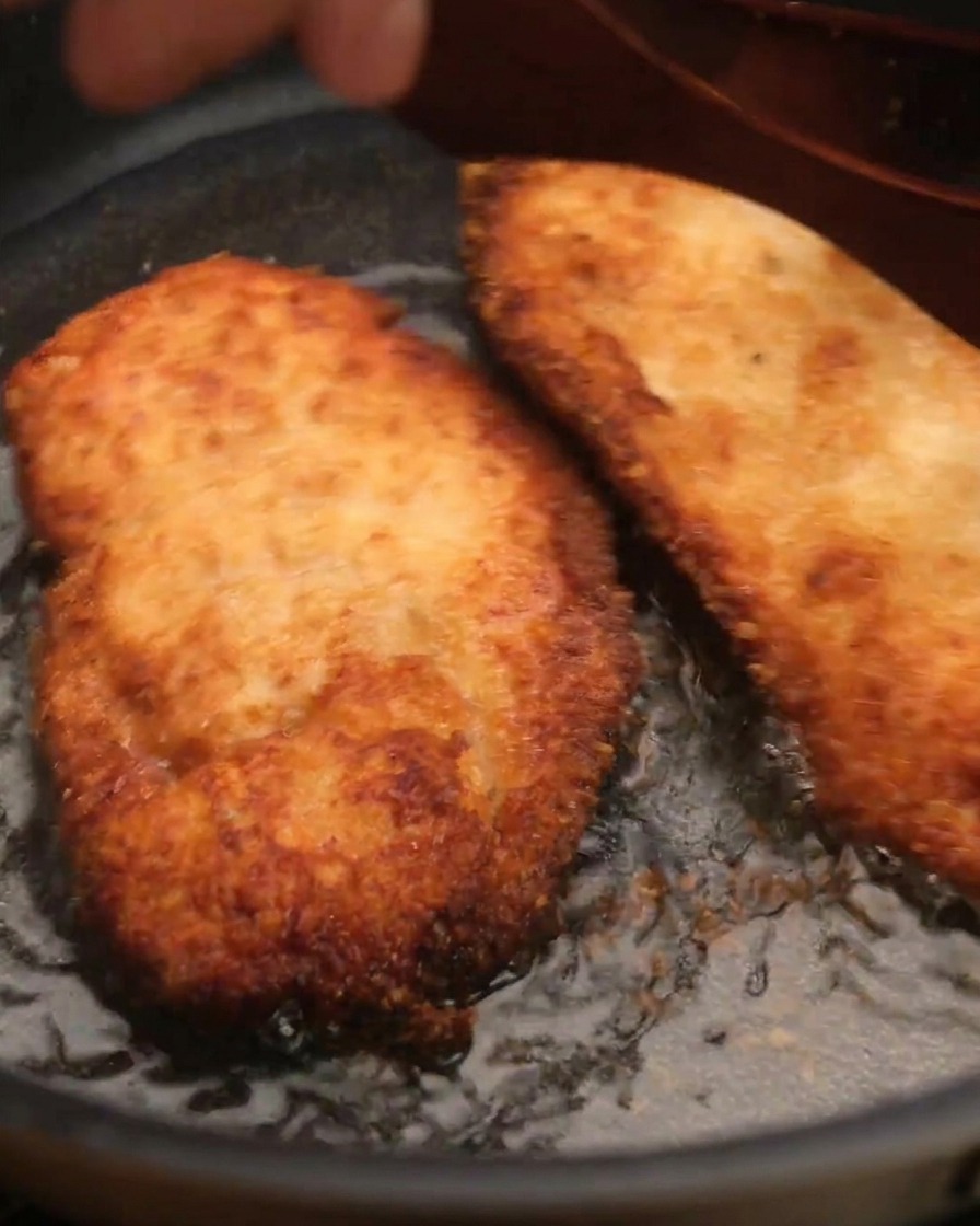 Pezzo di pollo fritto croccante sollevato dalla padella con una spatola di legno.