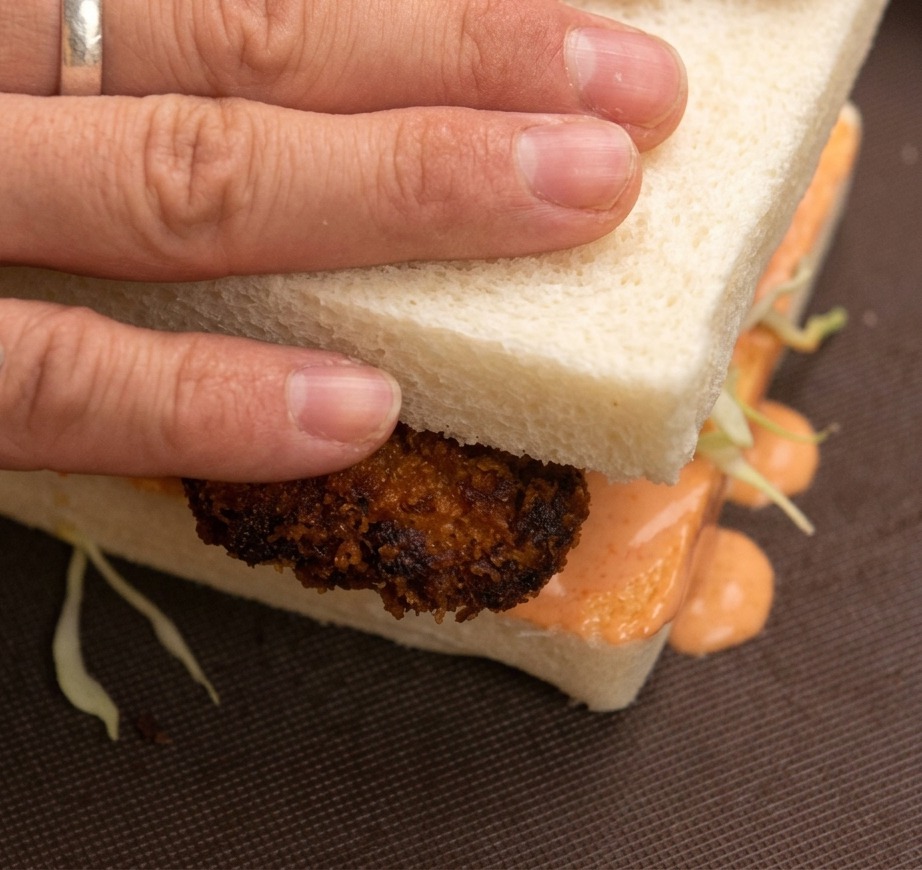 Mani che premono sulla fetta superiore del sandwich al pollo fritto.