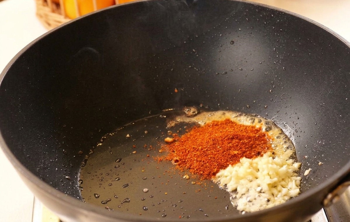 Aglio tritato e peperoncino nellolio caldo allinterno di un wok nero.