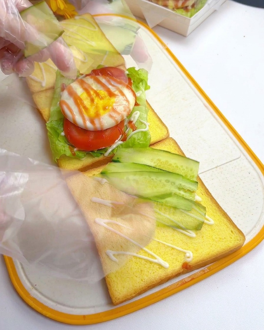 Mani che dispongono sottili fette diagonali di cetriolo fresco su una fetta di pane per toast.