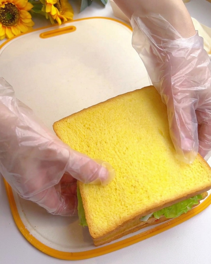 Due mani che premono sulla fetta superiore di pane, completando un sandwich alto e stratificato.
